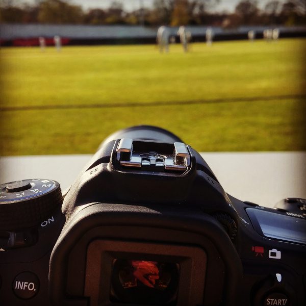 digital camera on a table at a cricket match (with the out of focus cricket going on in the background)