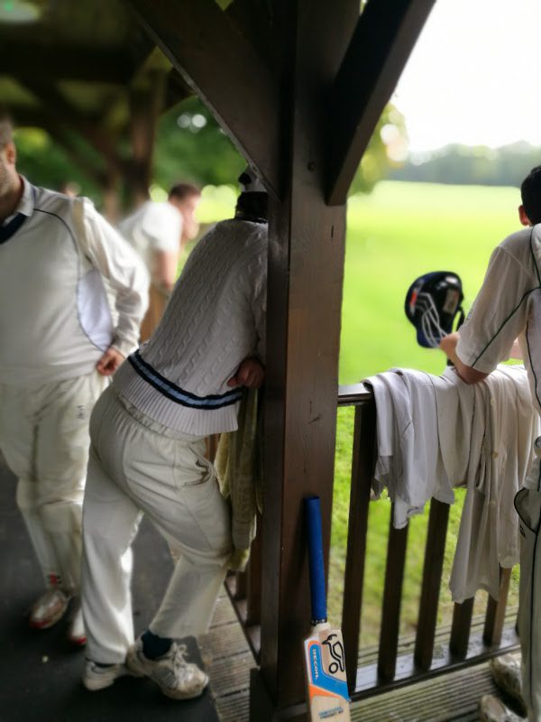 cricket club pavilion, players rest on the wooden rail outside
