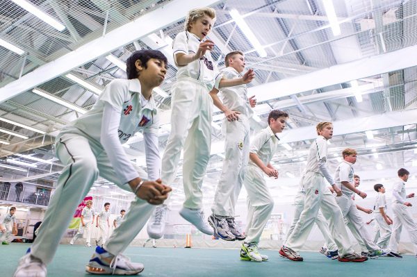 junior cricketers in whites train indoor, photo taken from floor angle looking up as they do jumps