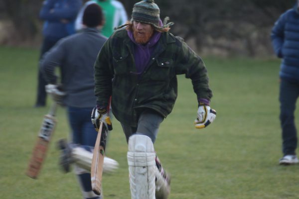 man runs between the wickets in jacket and wooley hat during a cricket match in the yorkshire dales