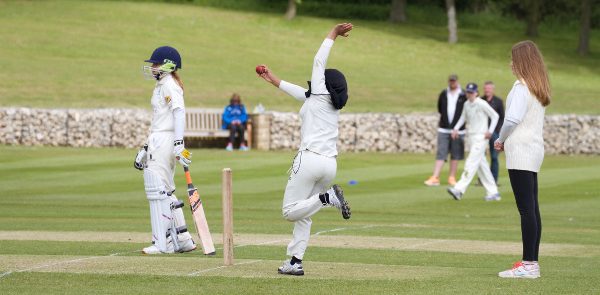 girls-cricket bowler in a cricket match delivers the ball, as the umpire watches on