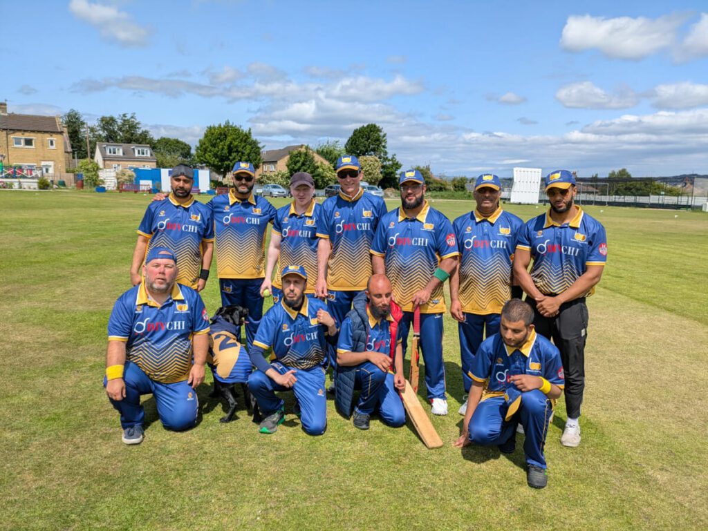 The Bradford VICC team pose for a team photo in their blue shirts with yellow collar and new blue caps. Sasha, Shah's dog, is wearing her own shirt too.