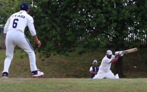 A right-handed batter hits a square drive while the fielder, at point, dressed in whites gets ready to react.